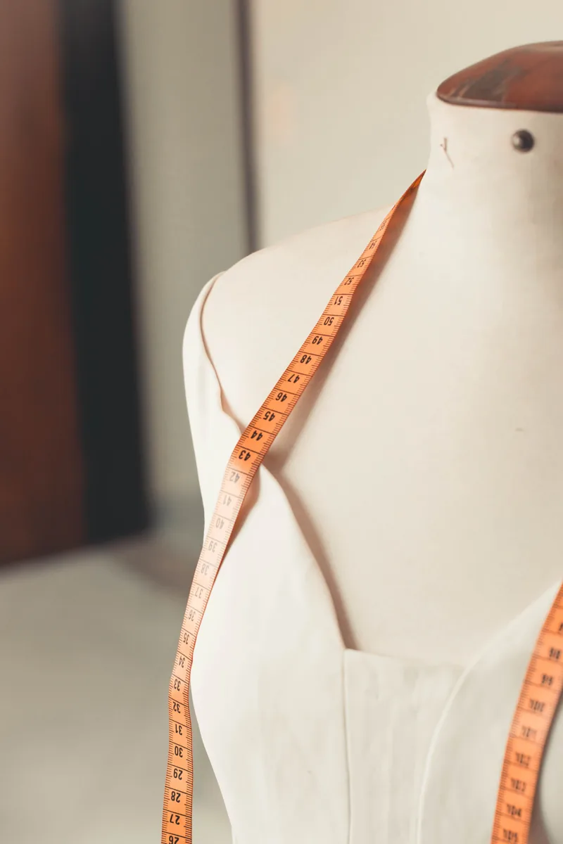 A dress form with a measuring tape draped over its shoulder
