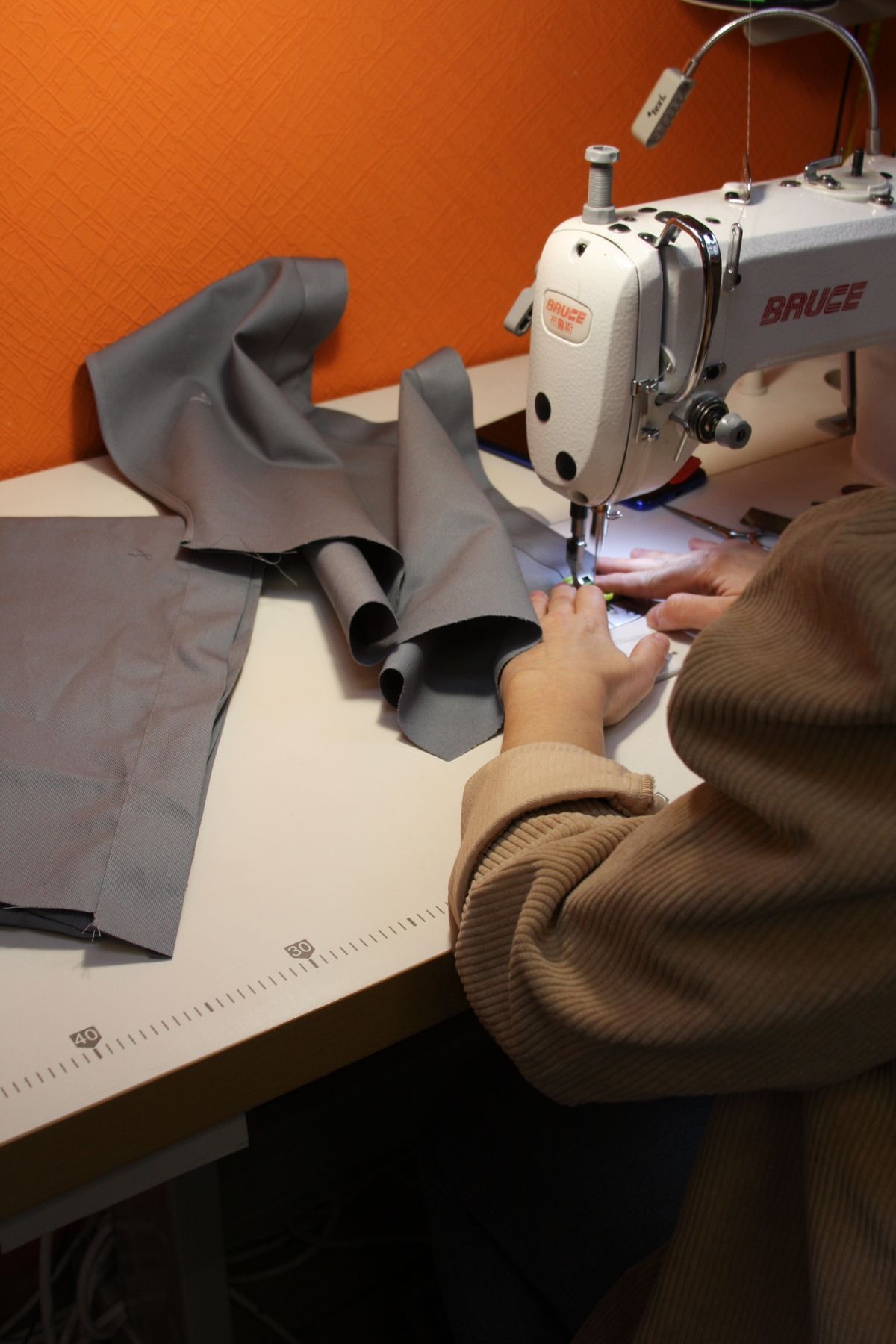 Hands guiding grey fabric beneath the needle of a sewing machine